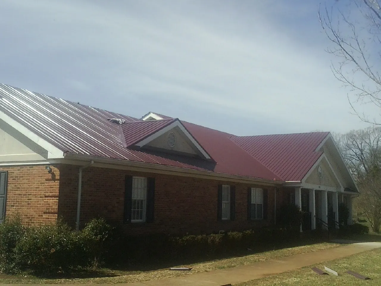 Red metal roof with gabled entries on a long brick building, from a Hail Damage Roof Repair job in Jamestown